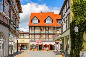 Um edifício europeu tradicional com telhado de telhas vermelhas, várias janelas e uma loja no andar térreo.