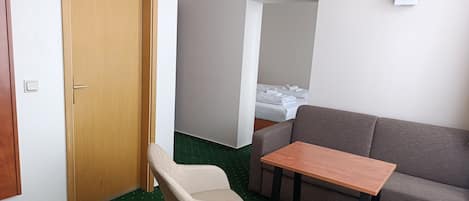 A room with a wooden door, a green carpet, a grey sofa, a small table, and a chair.