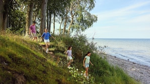 A group of people walking along a grassy hillside with a beach and ocean in the background.
