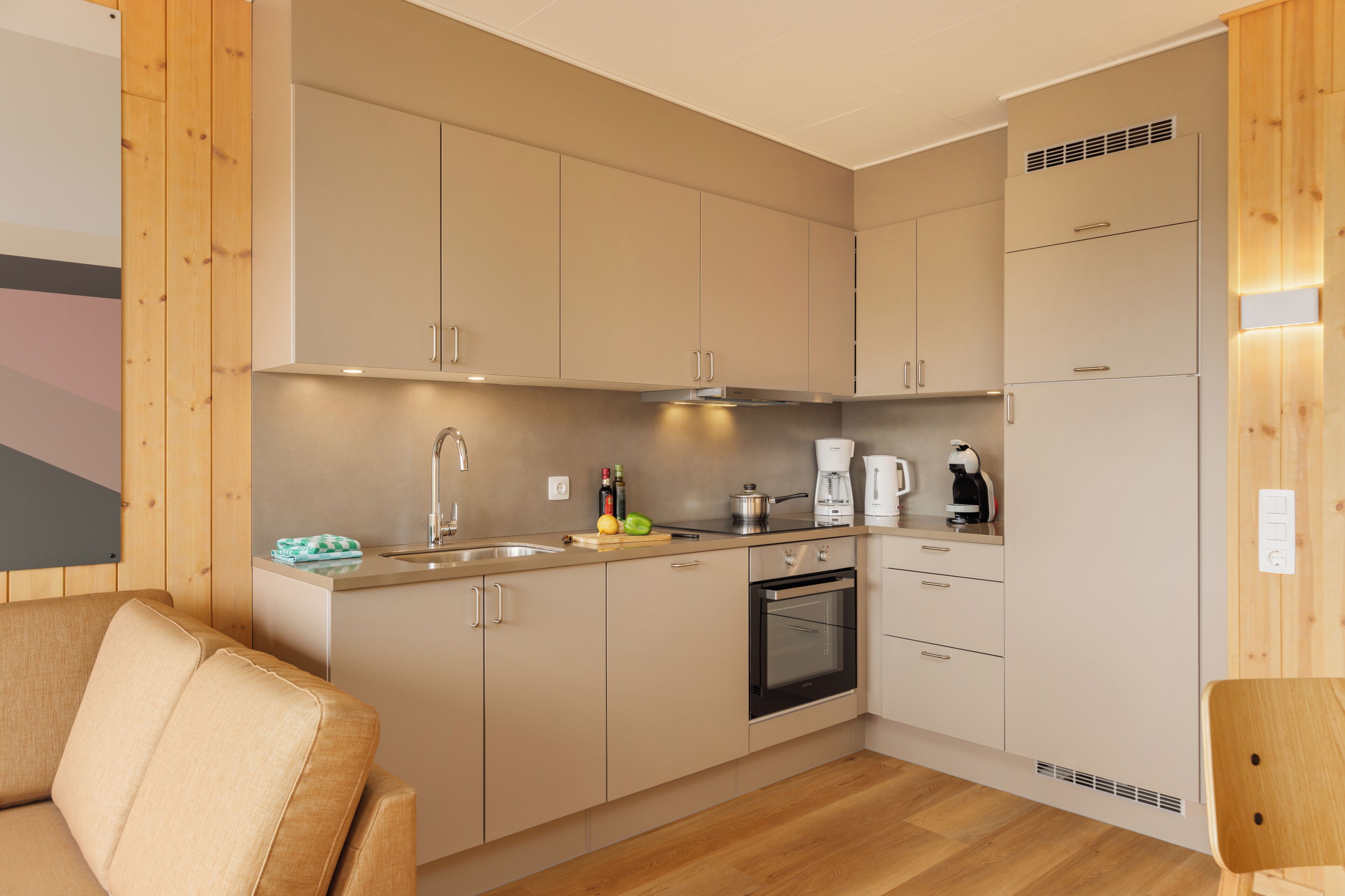 Eine moderne Küche mit Holzschränken, einem eingebauten Backofen und einer Kaffeemaschine.