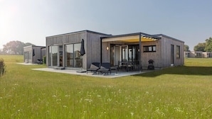 A modern house with a patio area, large windows, and a grassy field in the background.