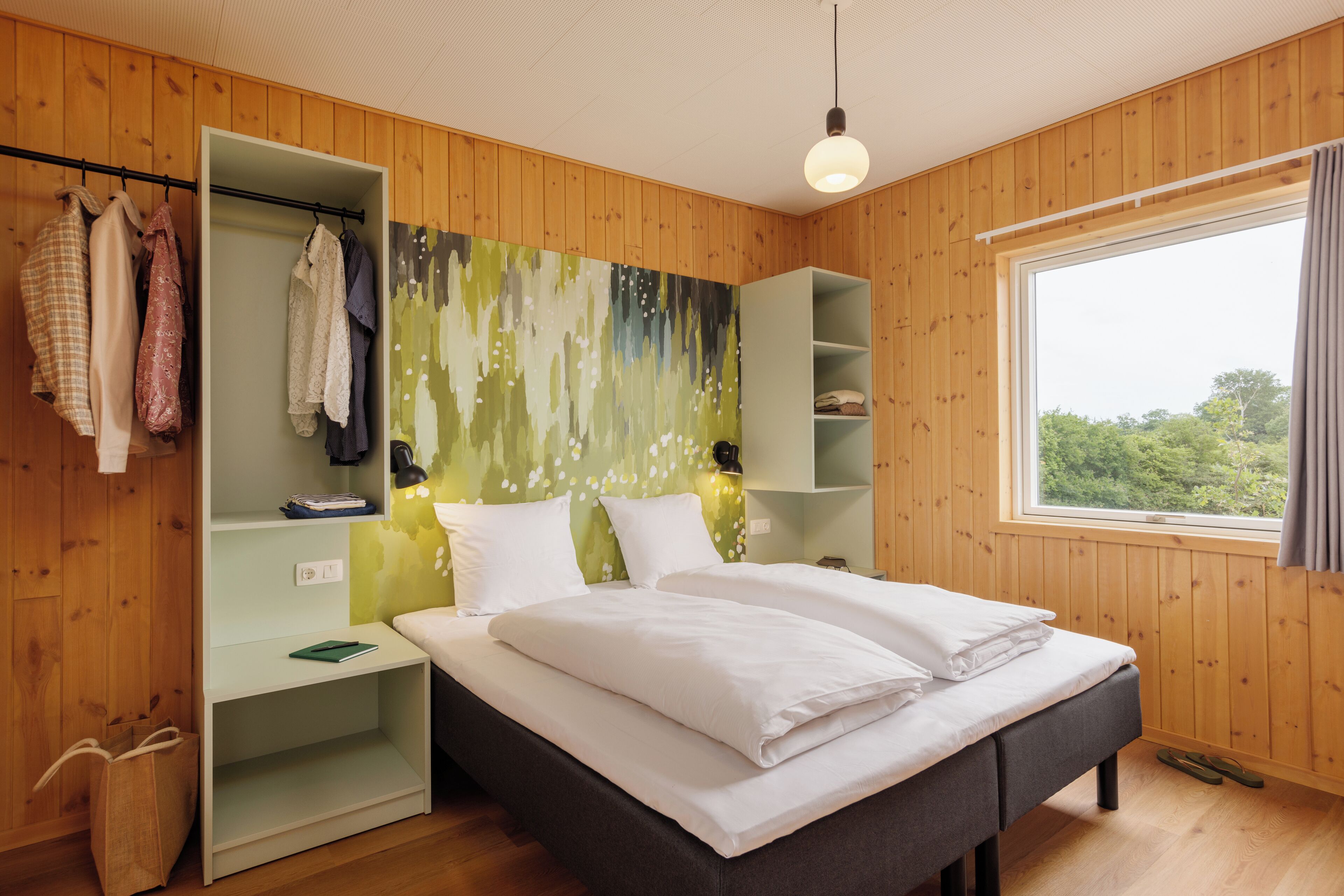 A bedroom with a bed, wooden walls, a window, and a wardrobe.