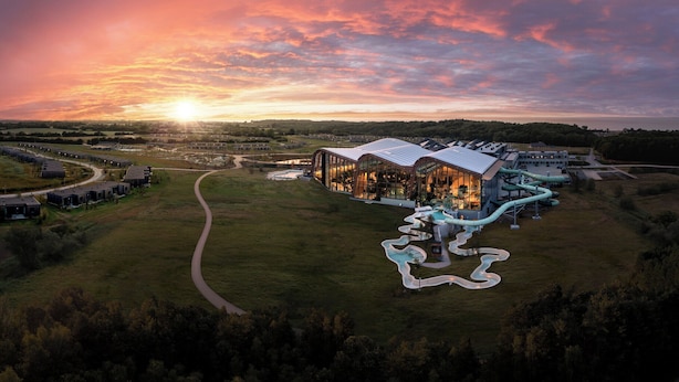 A large, modern building with a curved roof and glass facade, surrounded by a well-maintained lawn and a winding water feature.