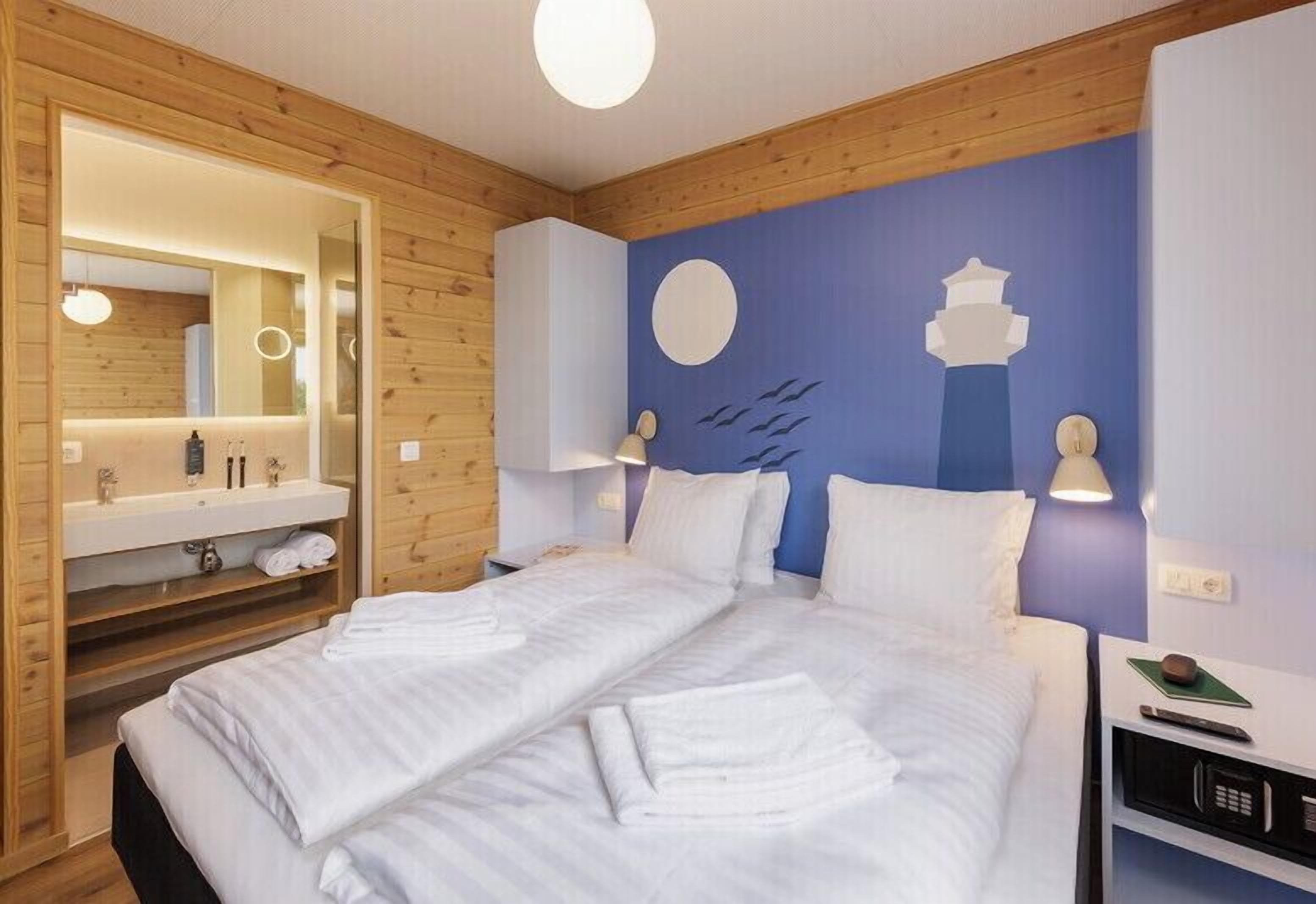 A hotel room with a wooden interior, a large bed with white linens, a built-in vanity with a mirror, and a wall with a blue and white design.