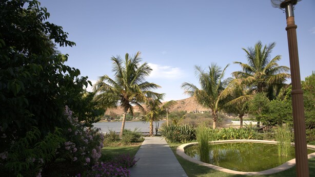 A pathway leading to a body of water with palm trees and a lamp post. - YAAN Bagela Villa (Udaipur)