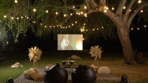 An outdoor movie night setup with a large screen, bean bags, and string lights under a tree. - YAAN Bagela Villa (Udaipur)