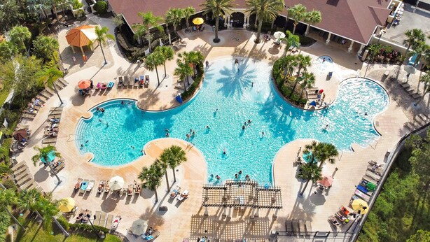 An aerial view of a resort with a large central pool, multiple lounge areas, and palm trees.