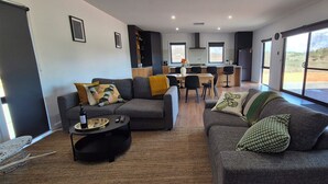 A modern living room with a sofa, a coffee table, and a dining area with chairs and a small kitchen in the background. - The Black House at Mannum (Mannum)