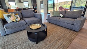 A modern living room with two grey sofas, a round black coffee table, and a large window offering a view of a hillside. - The Black House at Mannum (Mannum)