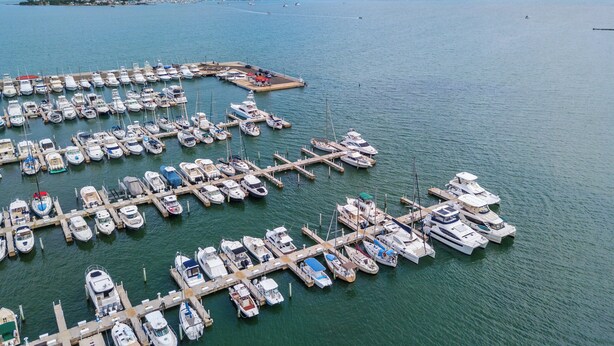 Een jachthaven met talloze boten aangemeerd aan steigers, een klein eiland met gebouwen op de achtergrond en een helder uitzicht op de zee.