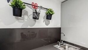 Een moderne keuken met een roestvrijstalen spoelbak, zwarte aanstaltinten en plantenbakken op een wandrek.