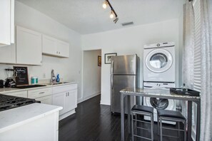 Una cocina moderna con armarios blancos, un refrigerador de acero inoxidable, una lavadora y un taburete de bar.