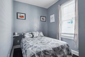 A bedroom with a bed, a window with curtains, and two framed pictures on the wall.