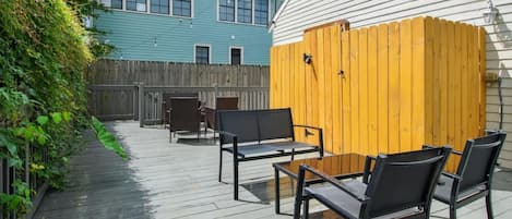 Un patio al aire libre con terraza de madera, sillas de metal y valla de madera.