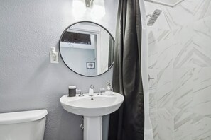 Un baño con un lavamanos blanco, un espejo redondo y una cortina de ducha.