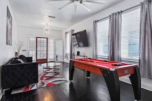 A modern living room with a pool table, a comfortable sofa, a television, and a ceiling fan.