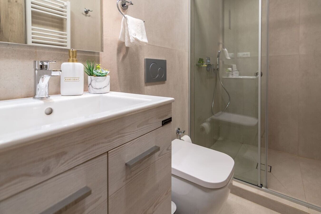 Et moderne badeværelse med en trækommode, et hvidt håndvaskarrangement, en glasbrusekabine og et toilet.