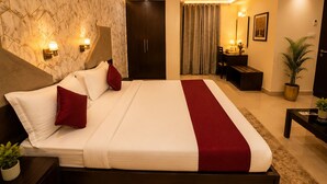 A hotel room with a large bed, a desk, a chair, a wardrobe, and a potted plant.