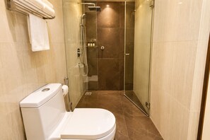 Et moderne badeværelse med et glasvægshus, toilet og et håndklædestativ.