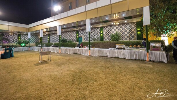 Un salón de banquetes al aire libre con mesas dispuestas para comer, rodeado por un seto bajo y una pared con diseño.