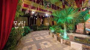 Un jardín interior con piso de cuadros, plantas colgantes y un candelabro.