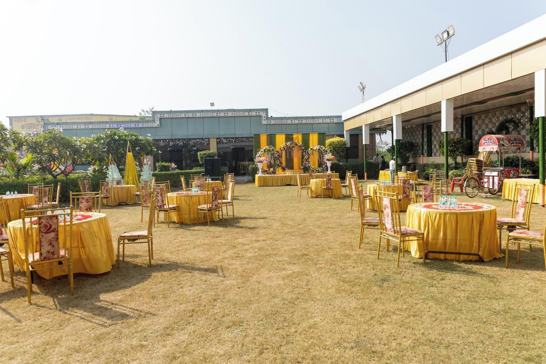 An outdoor event space with round tables and chairs, decorated with yellow tablecloths and floral arrangements.