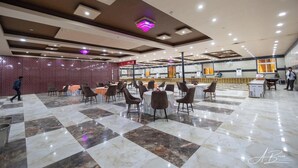 A spacious lobby with a checkered marble floor, multiple seating areas with round tables and chairs, a reception desk, and a decorative wall with a patterned design. - Royal Mansion Lawns (Kanpur)