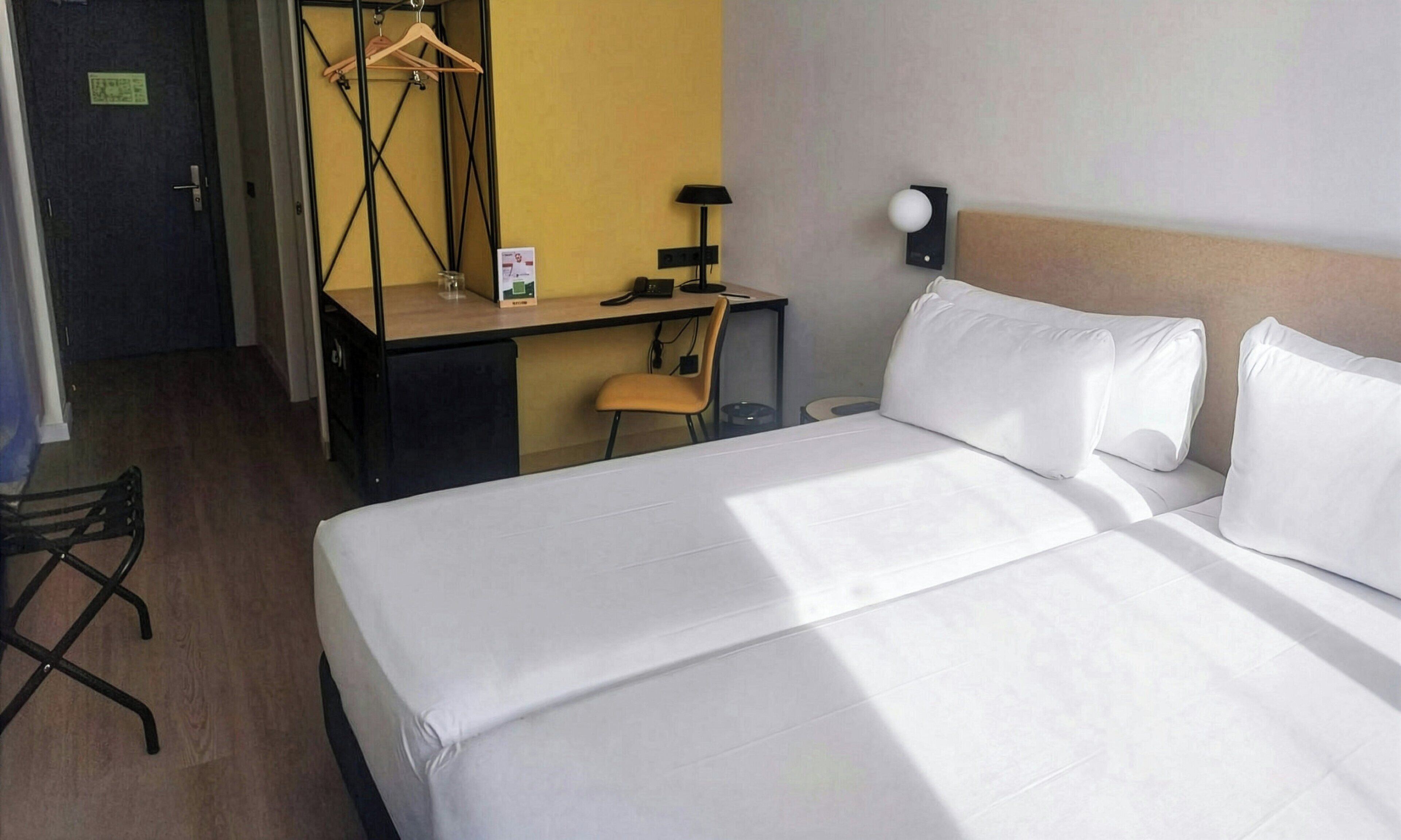Ein Hotelzimmer mit Bett, Schreibtisch, Stuhl, Lampe und Kleiderhaken.
