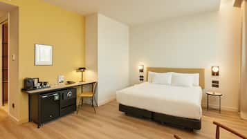 Habitación de hotel con cama, escritorio, silla y una mesita de noche con lámpara.