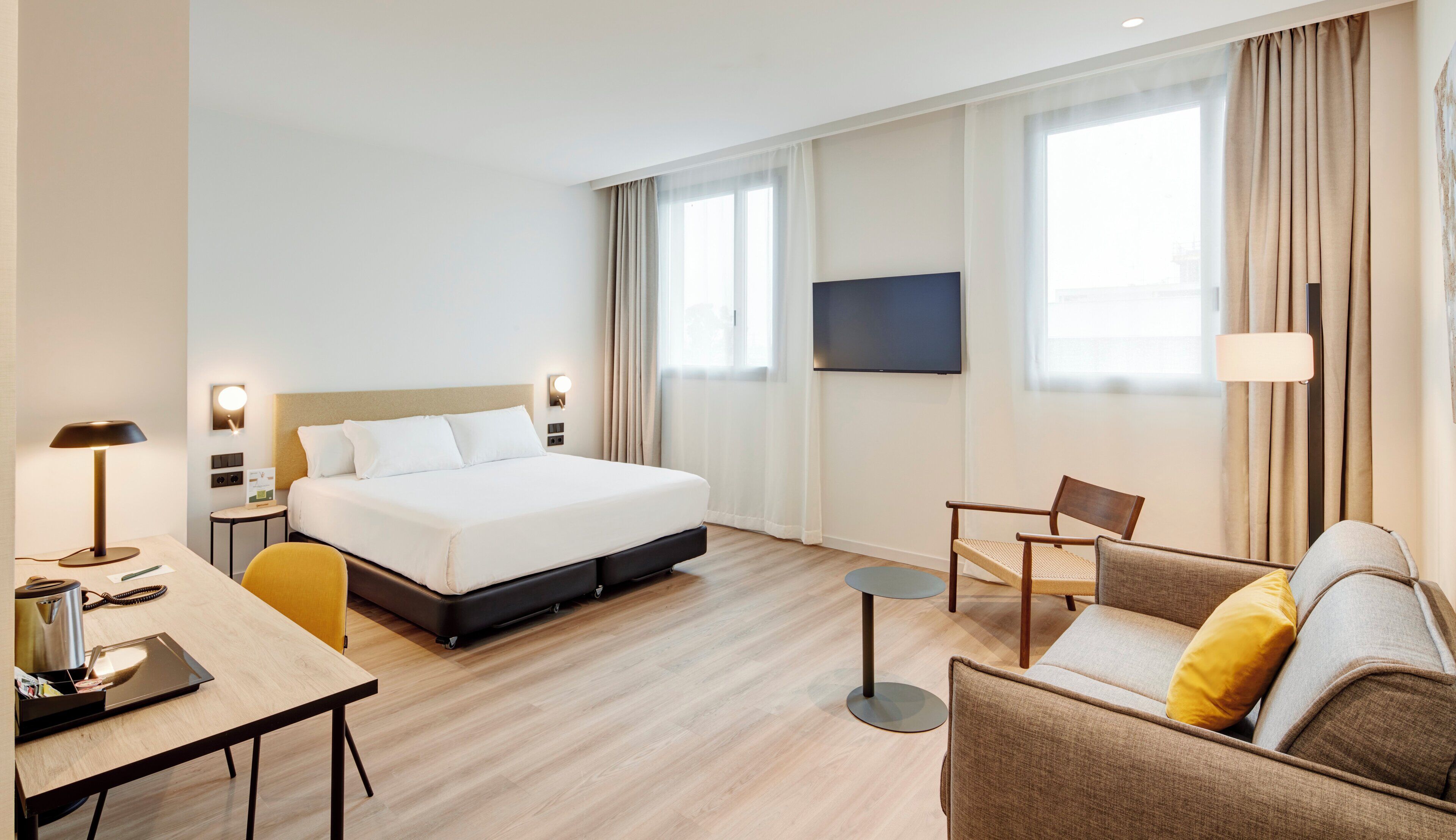 A hotel room with a bed, a desk, a chair, a sofa, and a TV.