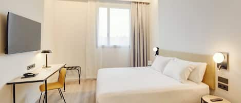 A hotel room with a bed, a desk, a chair, a TV, and a window with curtains.