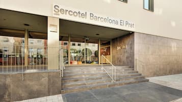 La entrada al hotel Mercotel Barcelona El Prat, con fachada moderna, puertas de cristal y una escalera que conduce a la entrada.