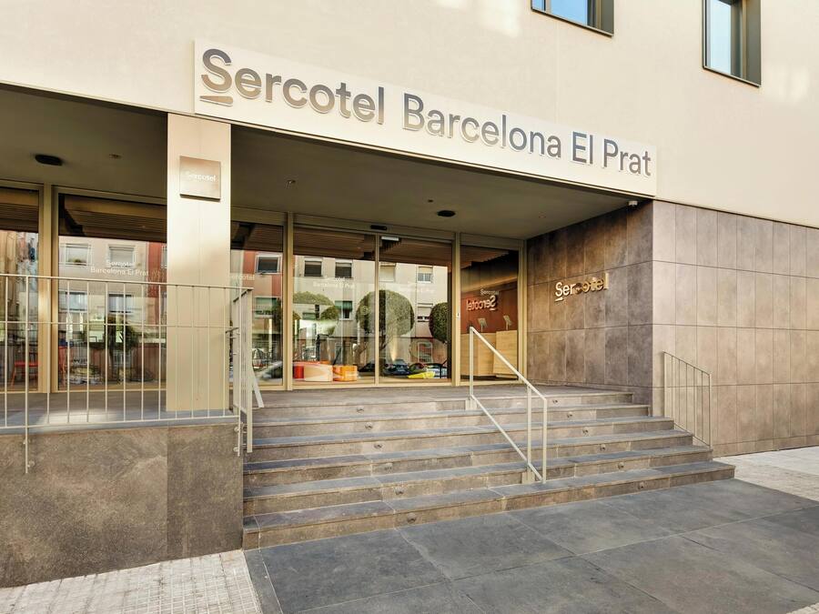 La entrada al hotel Mercotel Barcelona El Prat, con fachada moderna, puertas de cristal y una escalera que conduce a la entrada.