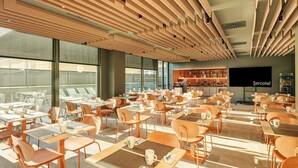 Een ruim café met veel tafels en stoelen, grote ramen en een zichtbare keuken.