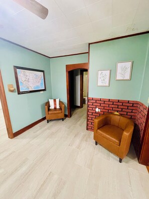 Una habitación con dos sillones de cuero, una puerta de madera, un mapa enmarcado y una pared decorada con ladrillos.