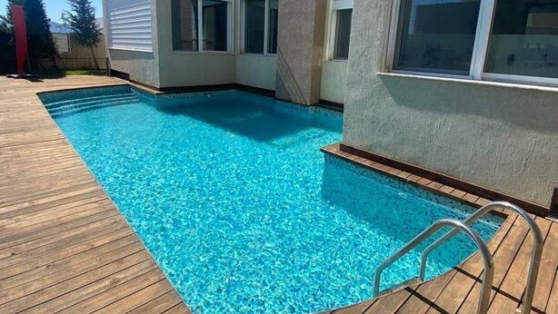 A modern house with a swimming pool, wooden deck, and large windows.