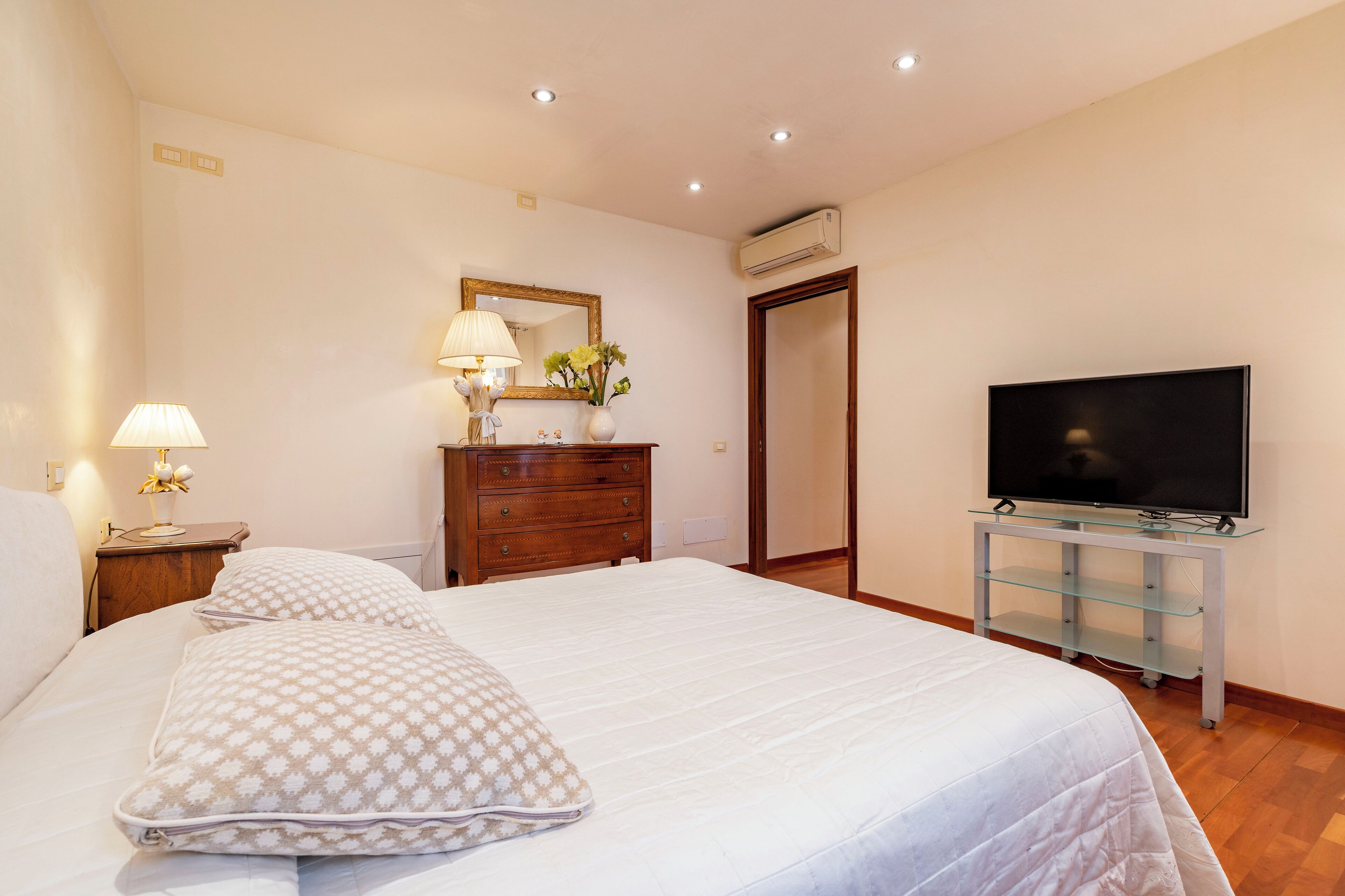 Een slaapkamer met een bed, een dressoir, een televisie en een spiegel.