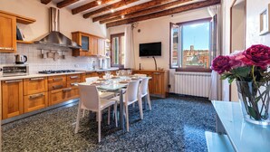 A modern kitchen with wooden beams, a dining area with white chairs, and a large window offering a city view. - Al Campanile View and Terrace by Wonderful Italy (Venice)
