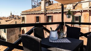 A balcony with wicker chairs and a table, a Monetto wine bottle, and a potted plant. - Al Campanile View and Terrace by Wonderful Italy (Venice)