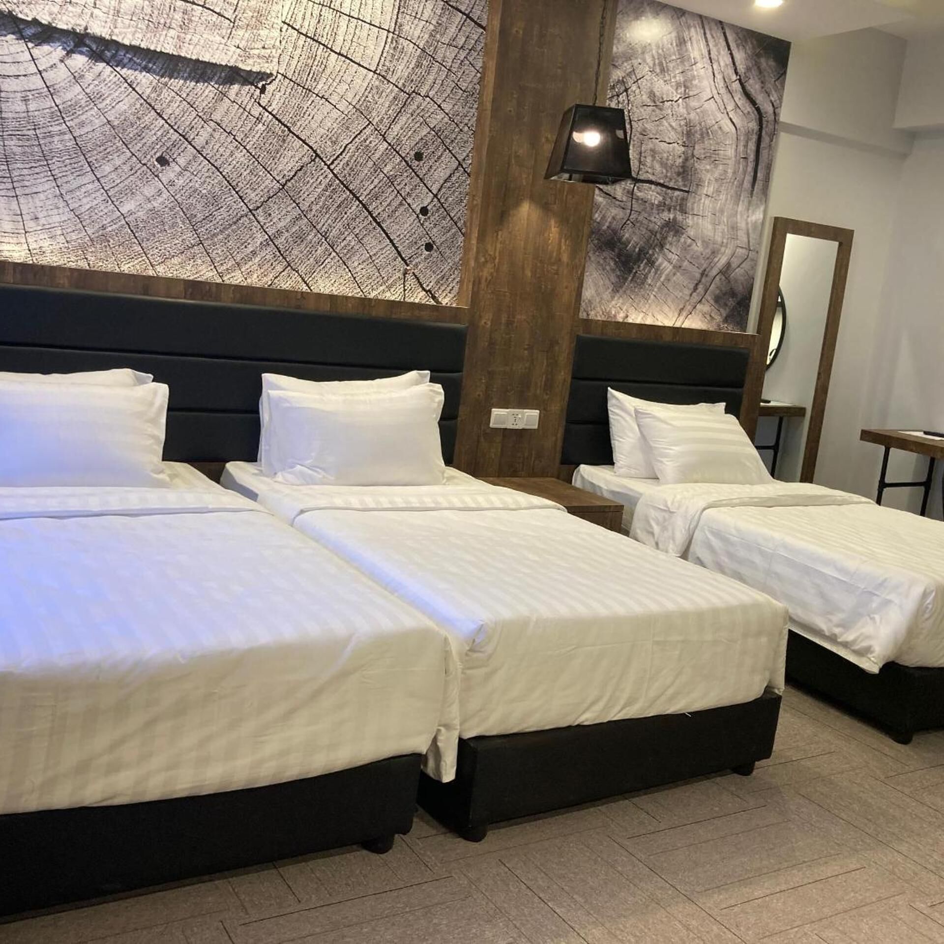 A hotel room with three beds, a large wall map, and a modern lamp.