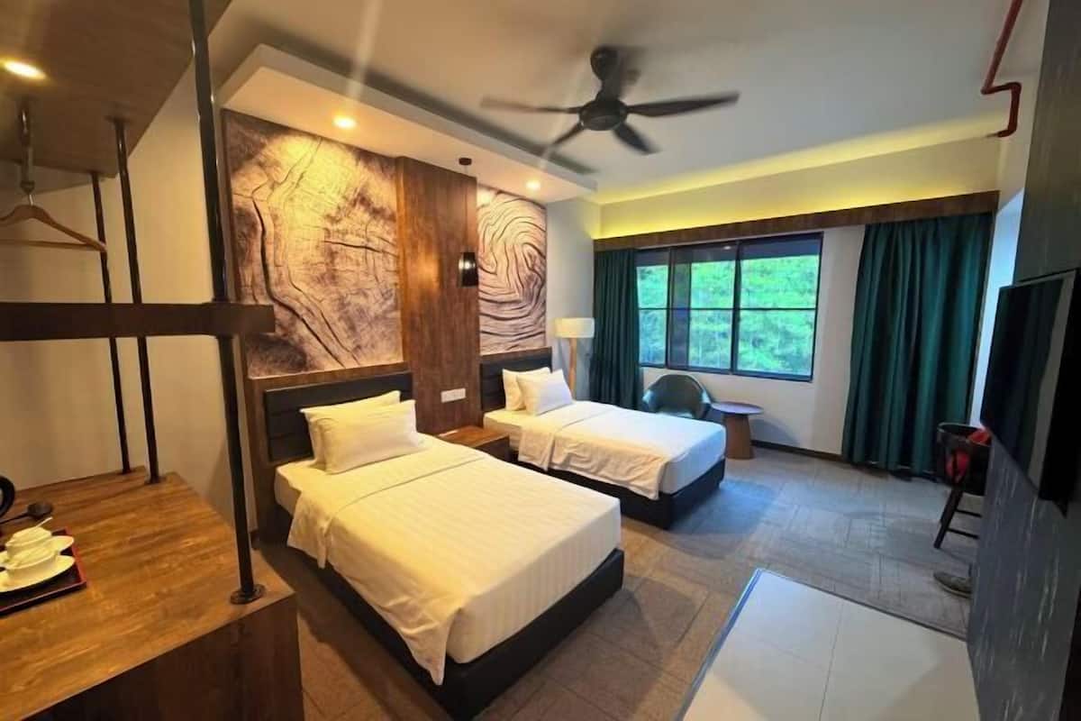 A hotel room with two beds, a wooden headboard, a large window with curtains, a ceiling fan, and a TV.