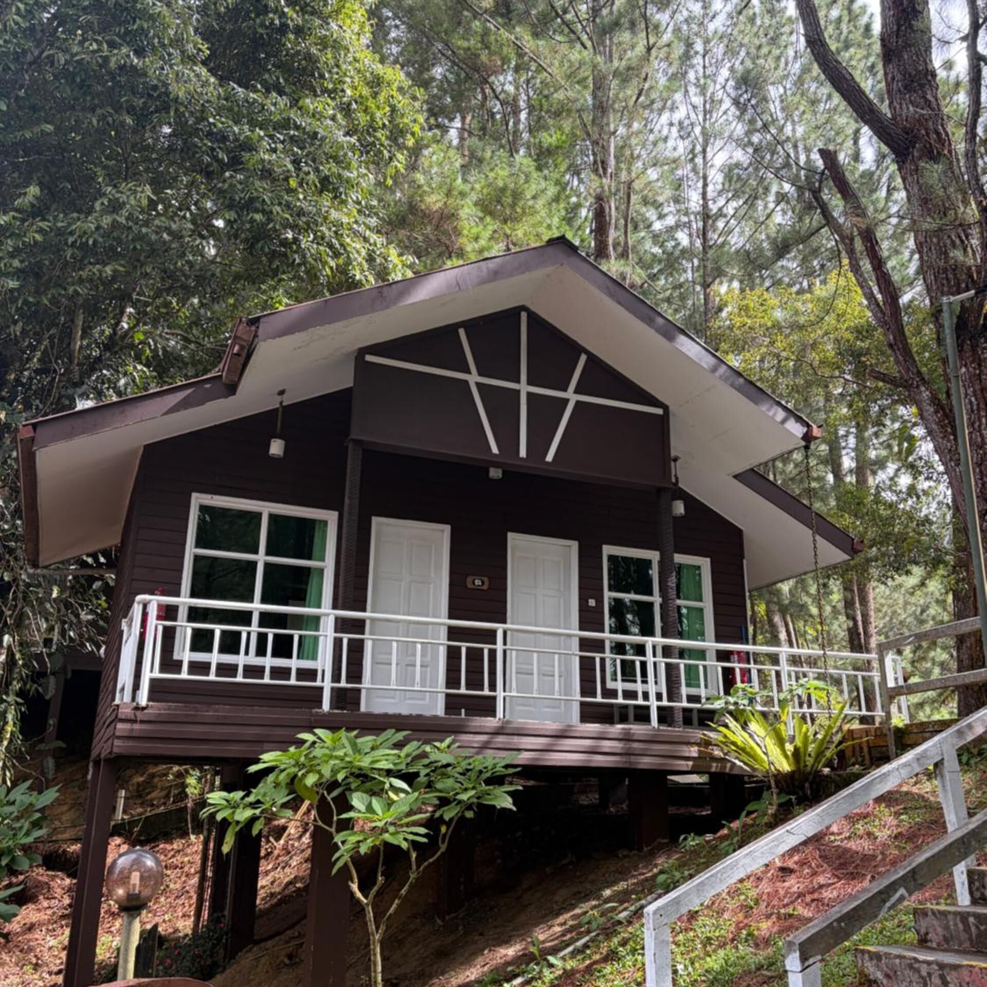 A two-story cabin with a balcony, surrounded by forest.