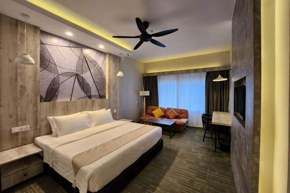 A hotel room with a large bed, a ceiling fan, a seating area with a sofa and table, and a TV.