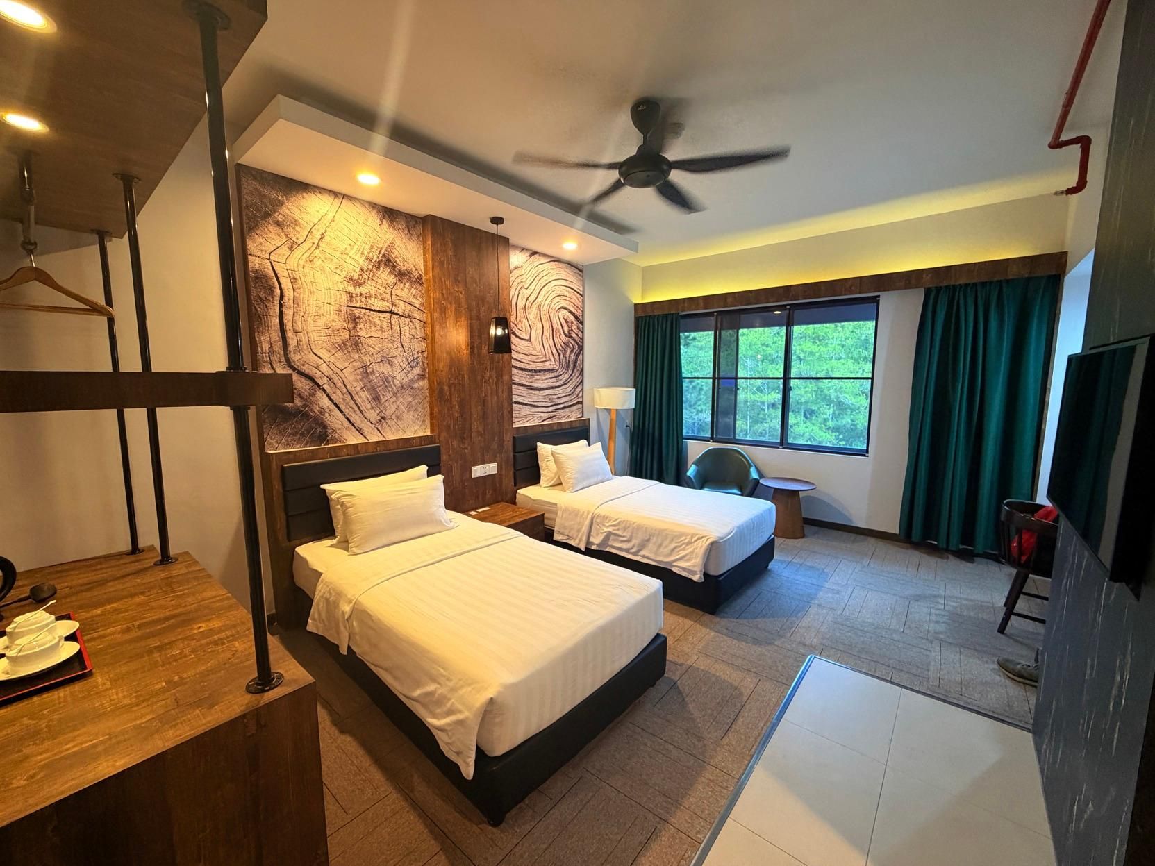 A hotel room with two beds, a desk with a tray of breakfast items, a ceiling fan, and a large window with curtains.