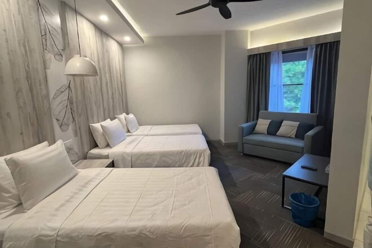 A hotel room with two beds, a sofa, a small table, a ceiling fan, and a window with curtains.