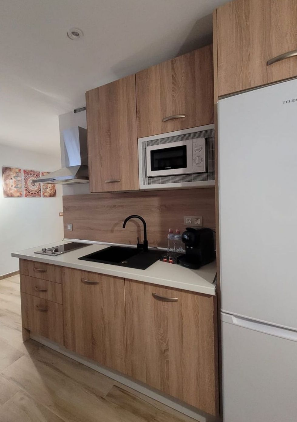 Eine Küche mit Holzausstattung, einer integrierten Mikrowelle, einem Spülbecken mit Armatur und einem Kühlschrank.