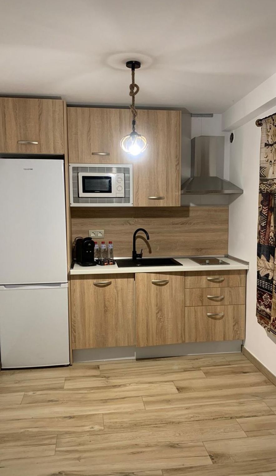 A compact kitchen with wooden cabinets, a microwave, a sink, and a gas stove.