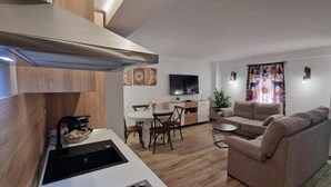 Une cuisine moderne équipée d’une cuisinière intégrée, un coin repas avec une table ronde et des chaises, un canapé et un téléviseur fixé au mur.