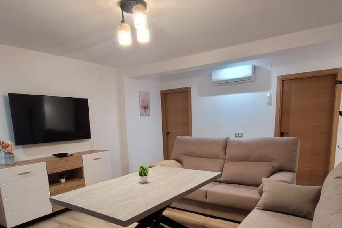 Ein modernes Wohnzimmer mit Fernseher, einem Holztisch, beigen Sofas und einem weißen Schrank.