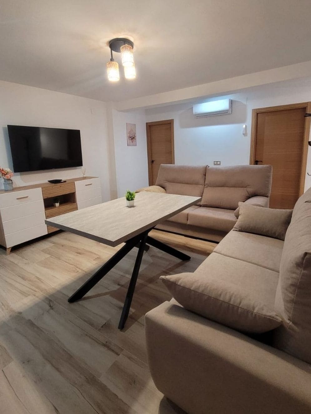 A modern living room with a flat-screen TV, a sofa, a coffee table, and a wooden cabinet.